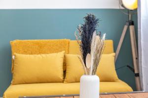 um sofá amarelo com um vaso com relva seca em L'ANTHRACITE, apartement rénové, tout confort em Saint-Jacques-de-la-Lande