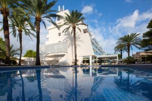 a swimming pool with palm trees in front of a building at Mar Hotels Playa de Muro Suites in Playa de Muro