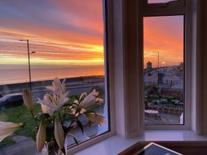 un jarrón de flores sentado en una ventana con una puesta de sol en 46 The Promenade en Withernsea