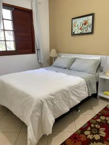 a bedroom with a large bed with white sheets and a window at Casinha aconchegante perto da praia Guarajuba - Ba in Guarajuba