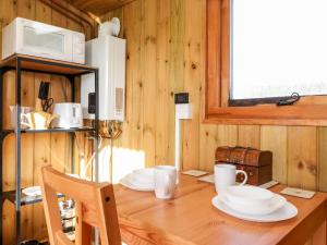 a kitchen with a wooden table with plates and a microwave at Maquessa Shepherd's Hut in Dumfries