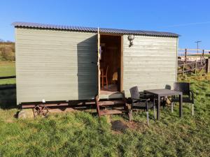 a shed with a table and chairs in a field at Maquessa Shepherd's Hut in Dumfries