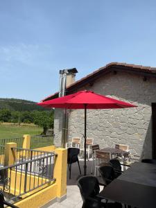 un patio con mesas, sillas y una sombrilla roja en Casa BellaTerra, en Villasana de Mena