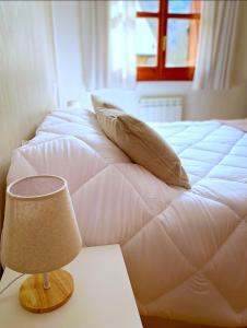 Una cama blanca con almohadas y una lámpara en una mesa. en CHECK-IN CASAS Ixarso, en Benasque