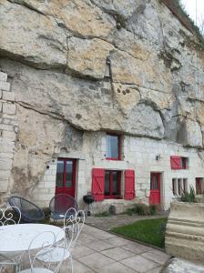 un edificio de piedra con puertas rojas y una mesa en Gite des Perreyeurs - maison troglodyte avec vue sur Loire en Montsoreau