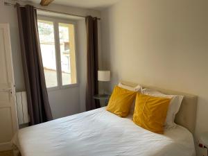 um quarto com uma cama com almofadas amarelas e uma janela em La Maison du Courtil, Amande-Olive em Moustiers-Sainte-Marie