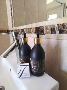 due bottiglie nere sedute sopra un lavandino del bagno di Goba Lodge a Gobabis
