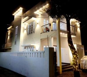 ein weißes Haus mit einem Baum davor in der Unterkunft Alleppy Whitefort Homestay Dulux Rooms with Balcony in Alappuzha