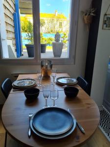a wooden table with plates and wine glasses on it at Marché Arago (3min), plage (8min), jardin clos. in Les Sables-dʼOlonne