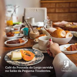 stół z talerzami jedzenia i osoba trzymająca filiżankę kawy w obiekcie Lofts do Largo w mieście Tiradentes