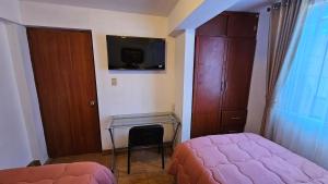 a bedroom with a bed and a desk and a tv at Los Profesionales - Hospedaje in Cusco