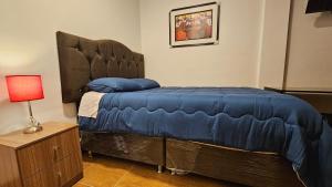 a bedroom with a bed with a blue comforter and a lamp at Los Profesionales - Hospedaje in Cusco