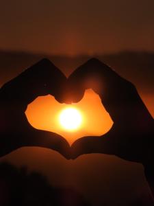 a silhouette of hands forming a heart with the sunset in the background at Chalés entre Nuvens in Campos do Jordão
