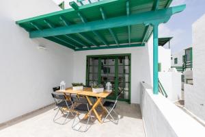 pérgola verde en un patio con mesa de madera y sillas en Casa Moure, en Costa Teguise