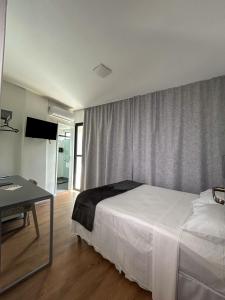 a bedroom with a white bed and a table and a window at Hotel do Vale in Campina Grande