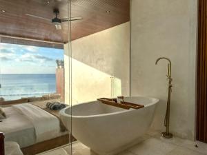 a bathroom with a tub and a bed with a view of the ocean at Mahi Mahi Beach Shack And Suites in Uluwatu