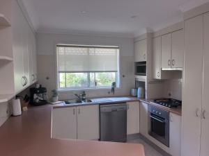 a kitchen with white cabinets and a sink and a window at Toowoon Bay - Private Pool - Outside Shower in Long Jetty