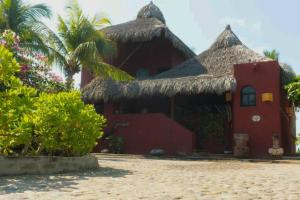 a red house with thatched roofs and palm trees at Casa de Playa Barra Vieja Acapulco in Barra Vieja