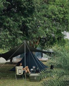 a woman sitting in a tent in the grass at ปิติฟาร์มมิลี่ คาเฟ่&แกลมปิ้ง ผามออีแดง in Ban Phumsaron