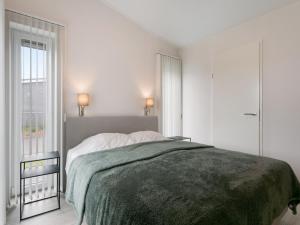 a white bedroom with a bed with a green blanket at Chalet in Zeeland by Scenic Pond in Wemeldinge
