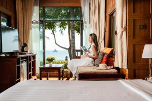 een vrouw die een boek leest in een kamer met een raam bij Koh Chang Paradise Resort & Spa in Ko Chang