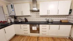 a kitchen with white cabinets and a stove top oven at Garland Lovely House with Garden, Watford in Bushey