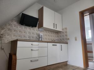 a kitchen with white cabinets and a tv on the wall at Ferienwohnung Auf der Heide in Großschönau