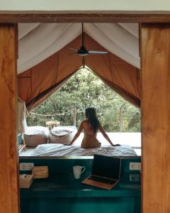 Eine Frau, die auf einem Bett in einem Zelt mit einem Laptop sitzt. in der Unterkunft Autentik Penida "Glamping" - Adults only in Nusa Penida