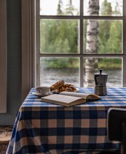 a table with a book and a cup of coffee and a window at Cabin by Byske river surrounded by the forest in Byske