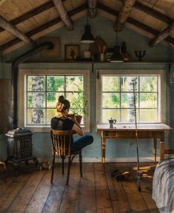 a woman sitting in a chair in a room with a table at Cabin by Byske river surrounded by the forest in Byske