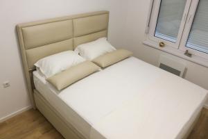 West Wing - Apartmani Živinice في Živinice: سرير بشرشف ووسائد بيضاء في غرفة النوم