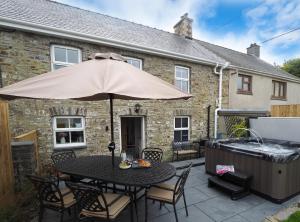 a patio with a table with an umbrella and a hot tub at Bryndalis Ciliau Aeron in Ciliau-Aeron