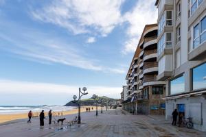 pessoas e um cão a passear numa praia com edifícios em Primera línea de playa con parking - Zarautz em Zarautz