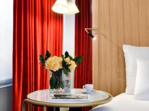 a vase of flowers on a table next to a bed at Hôtel l'Echiquier Opéra Paris - MGallery in Paris