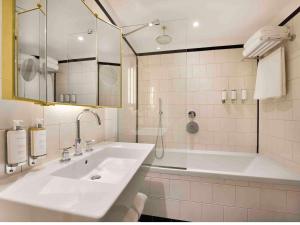 un bagno bianco con lavandino e vasca di Hôtel l'Echiquier Opéra Paris - MGallery a Parigi