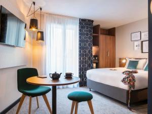 pokój hotelowy z łóżkiem, stołem i krzesłami w obiekcie Mercure Paris Montparnasse Pasteur w Paryżu