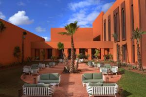 Doubletree By Hilton Ben Guerir Hotel & Residences في Benguerir: ساحة فيها كراسي والنخيل امام مبنى