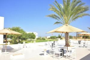 a patio with chairs and umbrellas and a palm tree at TMK Marine Beach - All Inclusive Seafront resort in Triffa