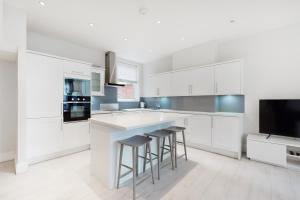 a kitchen with white cabinets and bar stools at Modern 3 Bed Apartment in Hampstead in London