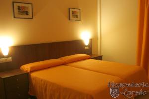 um quarto com uma cama com lençóis laranja e duas luzes em Hospedería Laredo em La Carlota