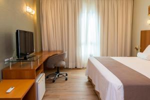 a hotel room with a bed and a desk with a television at Bourbon Convention Hotel Joinville in Joinville