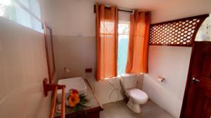 ein Bad mit WC und ein Fenster mit orangefarbenen Vorhängen in der Unterkunft Villa Paille en Queue in Flic-en-Flac