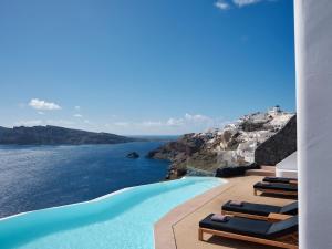Olvos Luxury Suites في أويا: حمام سباحة مع كراسي صالة تشايس والمحيط