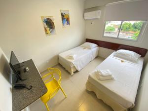a room with two beds and a desk and a television at NORTH HOTEIS in Montes Claros