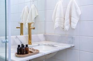 a white tiled bathroom with a sink and towels at Casa Hotel Sahy in Barra do Sahy