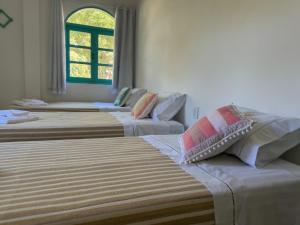 a group of three beds in a room with a window at Vila Rita Hostel Arraial d'Ajuda in Arraial d'Ajuda