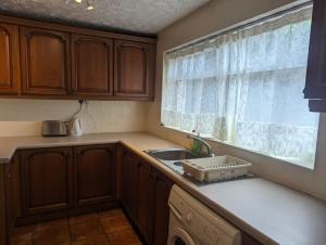 eine Küche mit Holzschränken, einem Waschbecken und einem Fenster in der Unterkunft Rooms close to City Centre in Beeston Hill