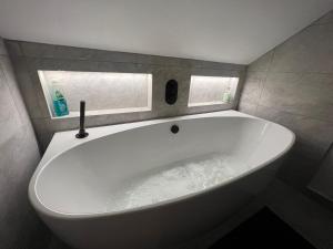 a large white tub in a bathroom with two windows at Seascape in Barton on Sea