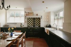 une cuisine avec des armoires noires et une table avec des chaises dans l'établissement Trinity Farmhouse - Stunning House & Gardens!, à North Cerney