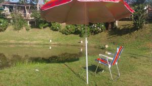 a chair sitting under an umbrella next to a pond at Pousada Beija flor in Extrema